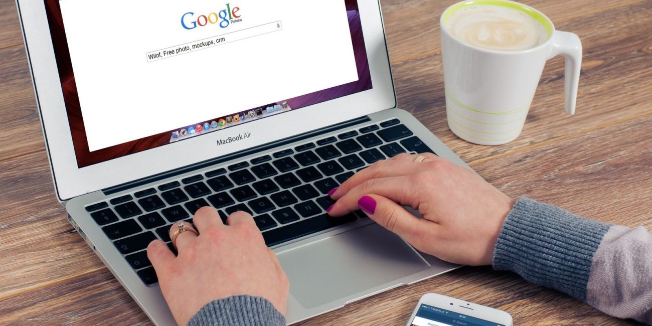 Hands typing on MacBook Air with Google search open, coffee nearby.