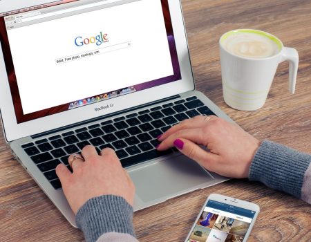 Hands typing on MacBook Air with Google search open, coffee nearby.